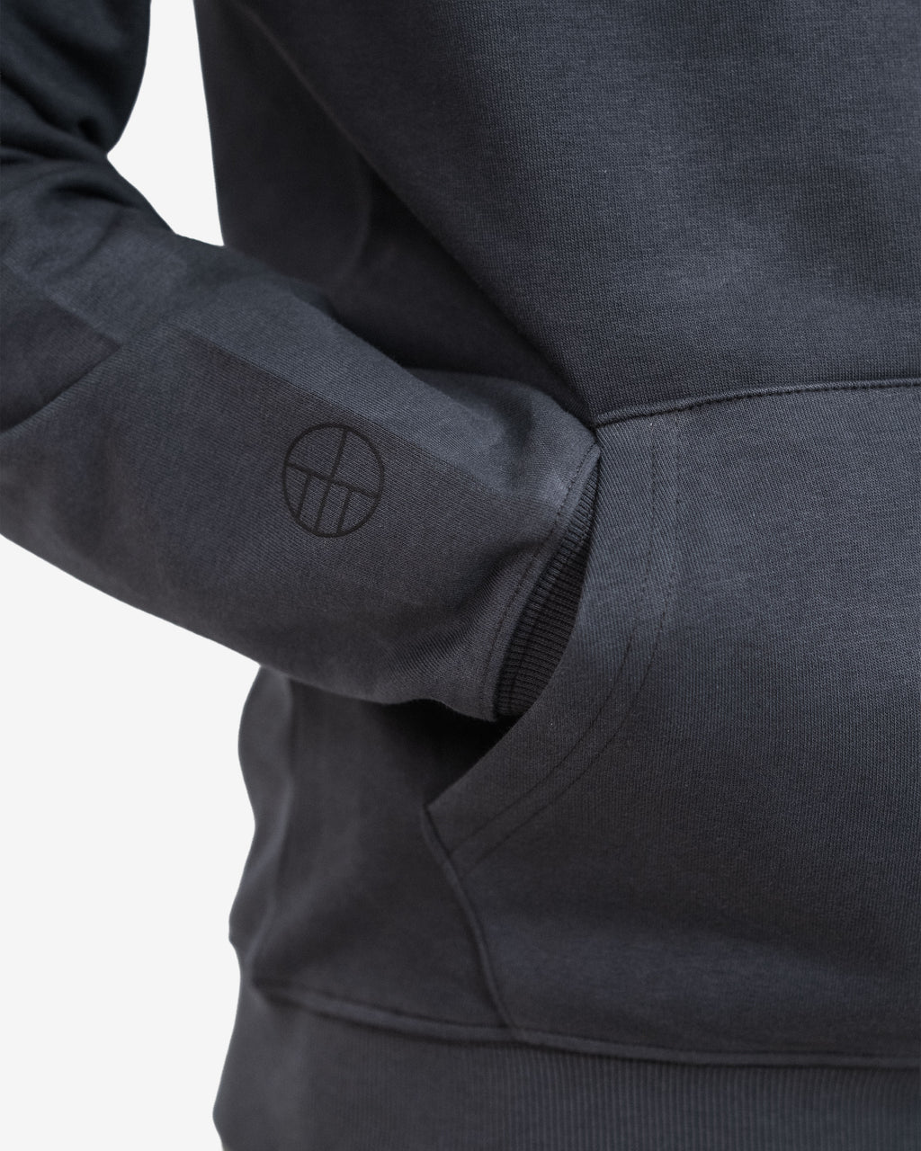 Close-up of a dark gray hoodie with a logo on the sleeve against a light gray background