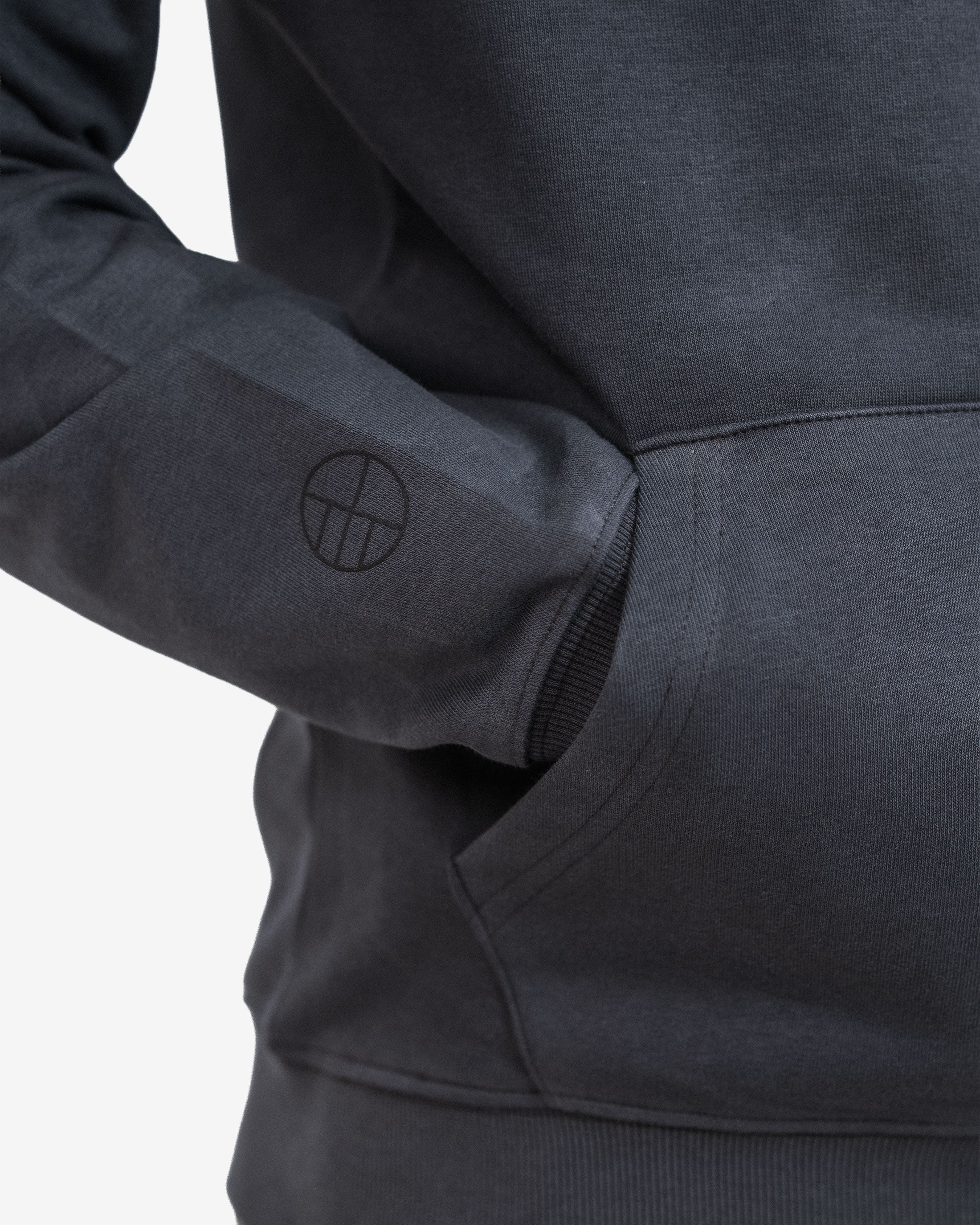Close-up of a dark gray hoodie with a logo on the sleeve against a light gray background
